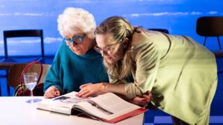 Anne Will Blankers en Lies Visschedijk staan voorovergebogen in een boek te kijken