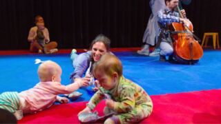 Kruipende baby's over de vloer en muzikant op achtergrond.