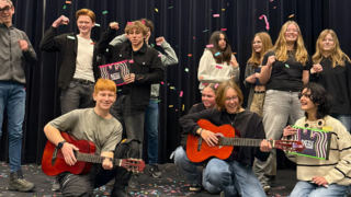 Een jonge band die juicht omdat ze mee mogen doen met Battle of the Schoolbands. Er is confetti. De twee voorste mensen hebben een gitaar vast.