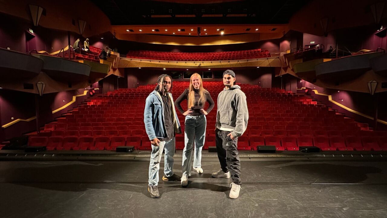 Drie mensen op foto in lege theaterzaal die kijken naar de camera