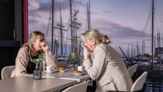 Twee vrouwen aan een tafeltje. Aan het genieten van koffie met een koek