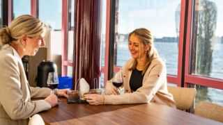 Twee vrouwen aan een tafel. ieder met een glas wijn en een portie bitterballen voor hen.