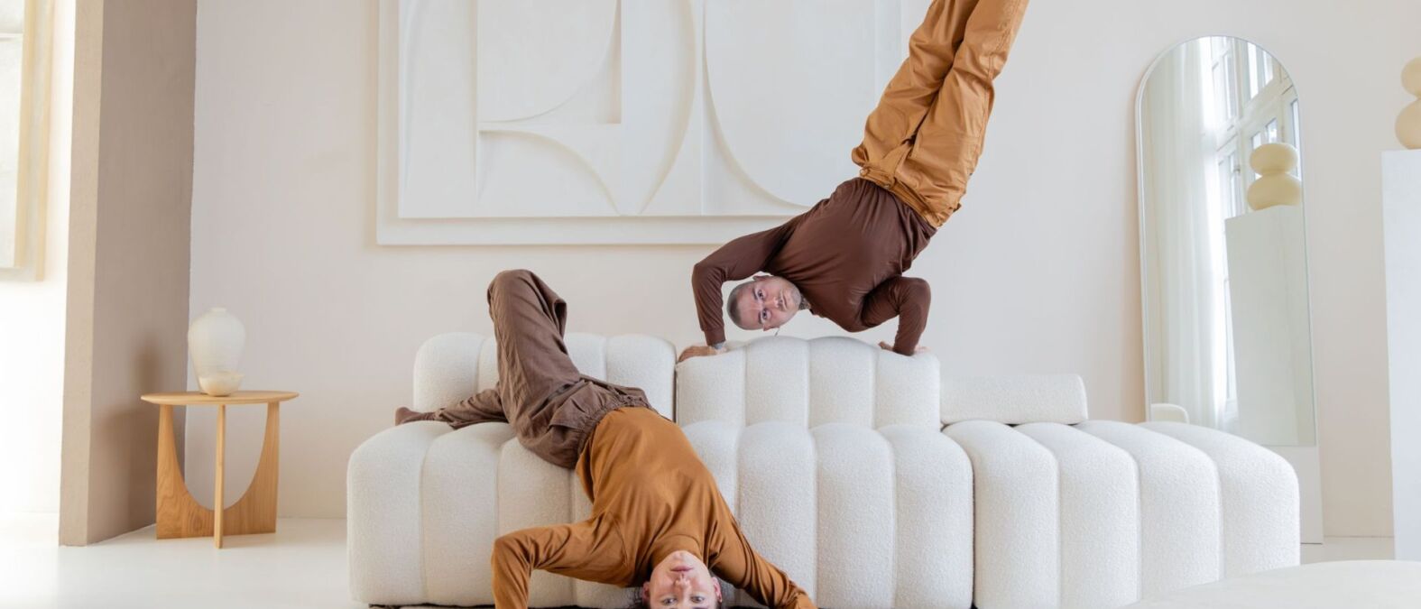 Twee dansers in bruine kleding doen een handstand op een bank en liggen op de bank