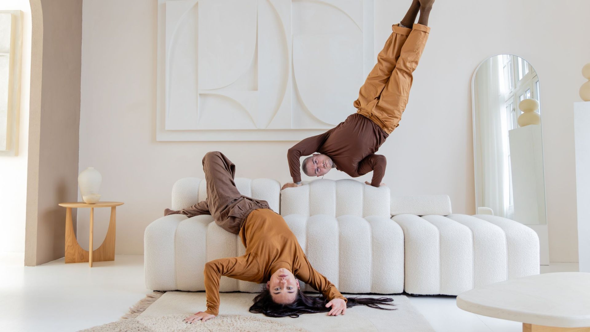 Twee dansers in bruine kleding doen een handstand op een bank en liggen op de bank