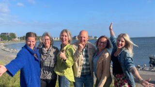 Zes enthousiaste Park-Ambassadeurs staan voor het markermeer en kijken vrolijk de camera in.