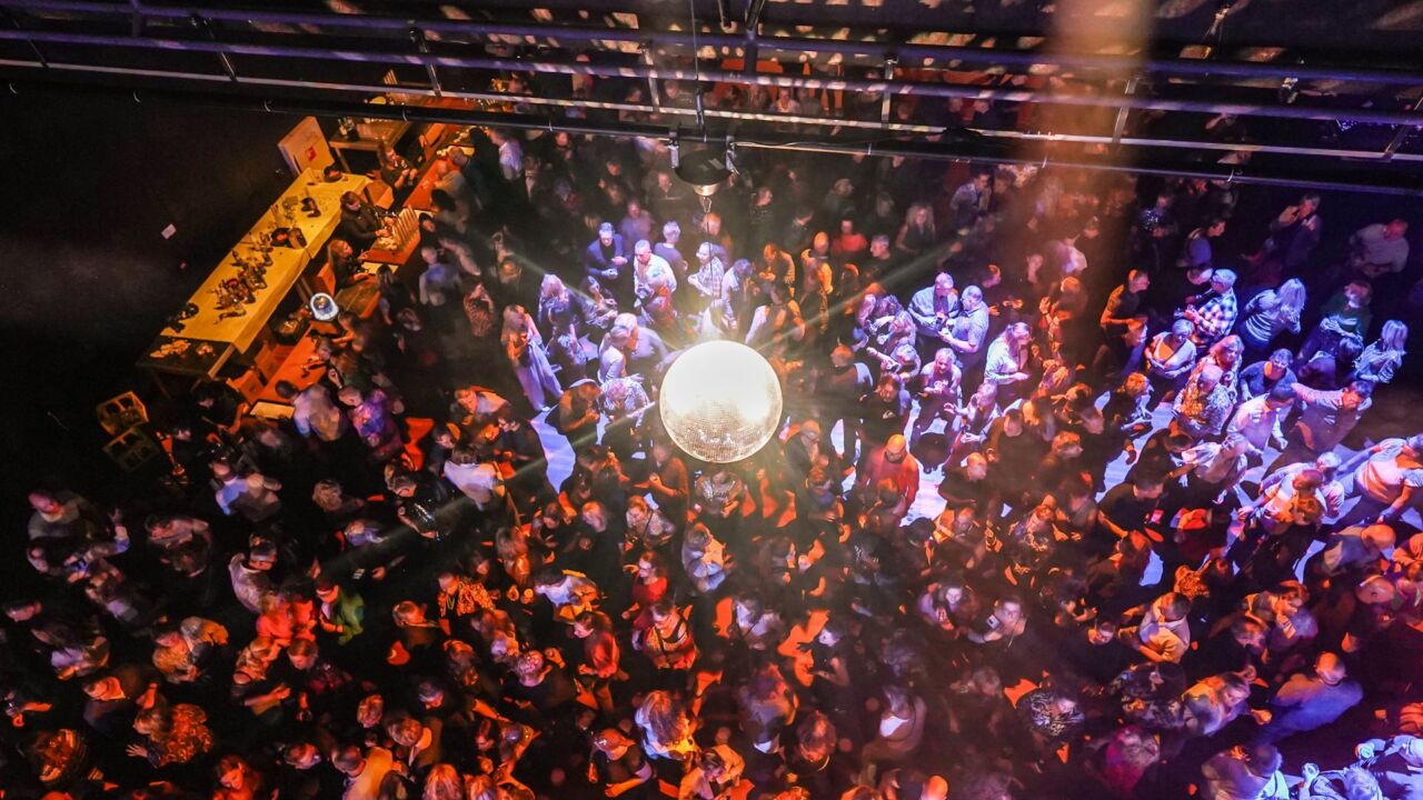 Dansende mensen in een feestzaal, met een grote discobal aan het plafond