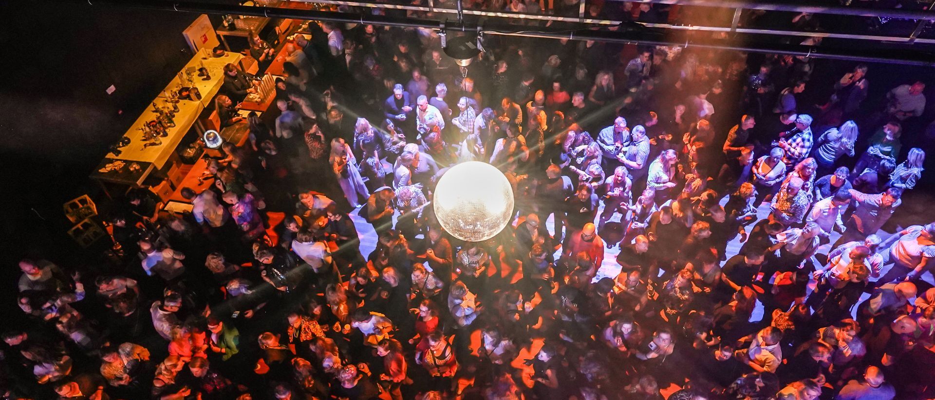 Dansende mensen in een feestzaal, met een grote discobal aan het plafond