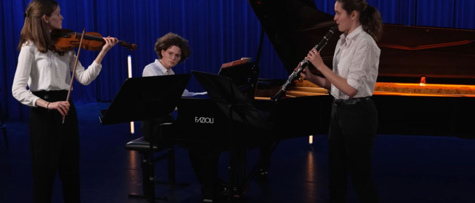 Backter Trio op piano, fluit en viool voor blauw gordijn.