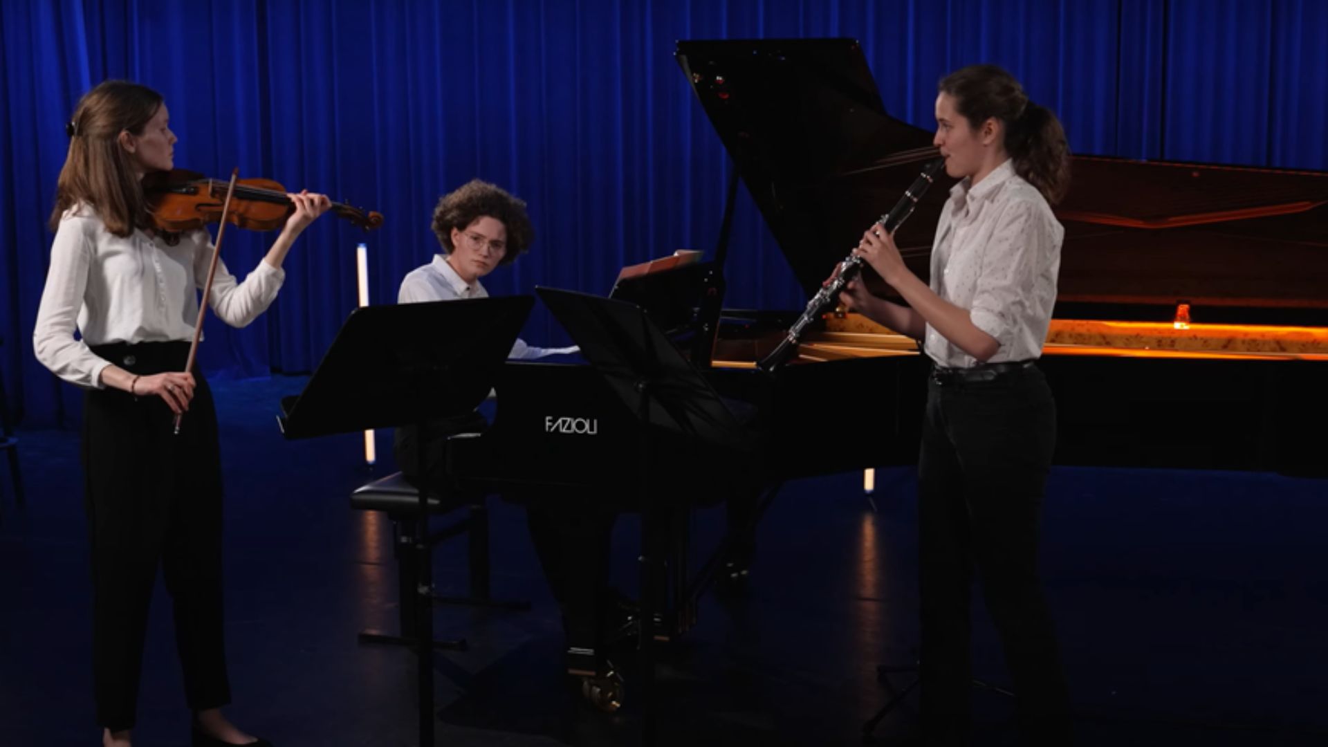 Backter Trio op piano, fluit en viool voor blauw gordijn.