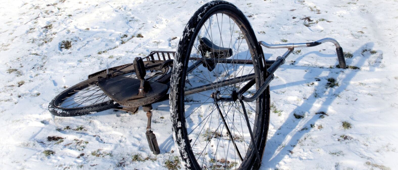 Een oude zwarte fiets ligt op zijn kant in de sneeuw