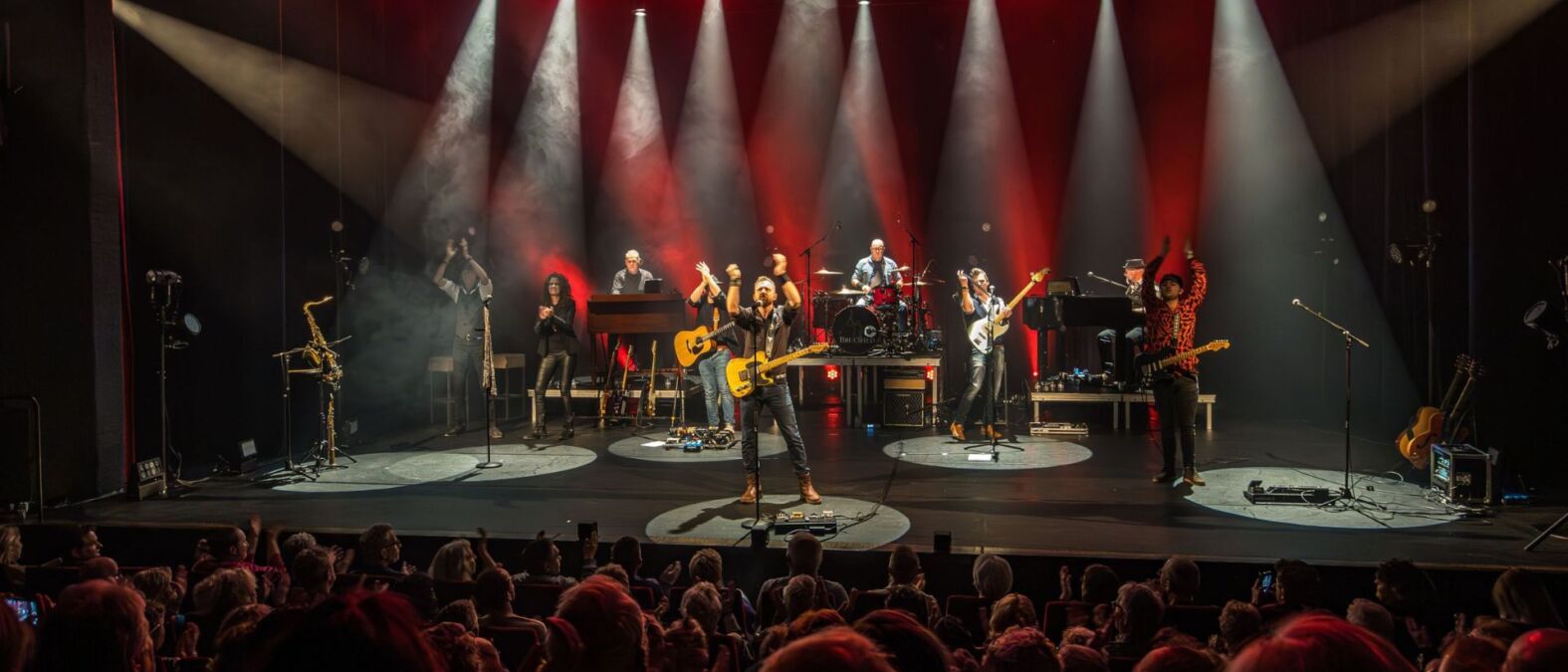 Een band van 9 mensen op het podium in met rode en witte lichten.