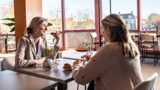 Twee vrouwen aan een tafeltje genieten van wat te drinken en wat te eten.