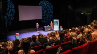 Twee presentatoren houden een presentatie voor een volle theaterzaal