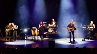 Een foto van The Cats Aglow Tribute op het podium terwijl ze aan het optreden zijn.