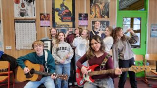 Schoolband van negen leerlingen met instrumenten in hun handen kijkend naar de camera