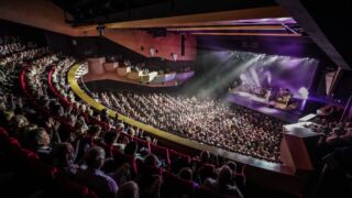 Een volle theaterzaal gezien vanaf het balkon tijdens een theaterconcert