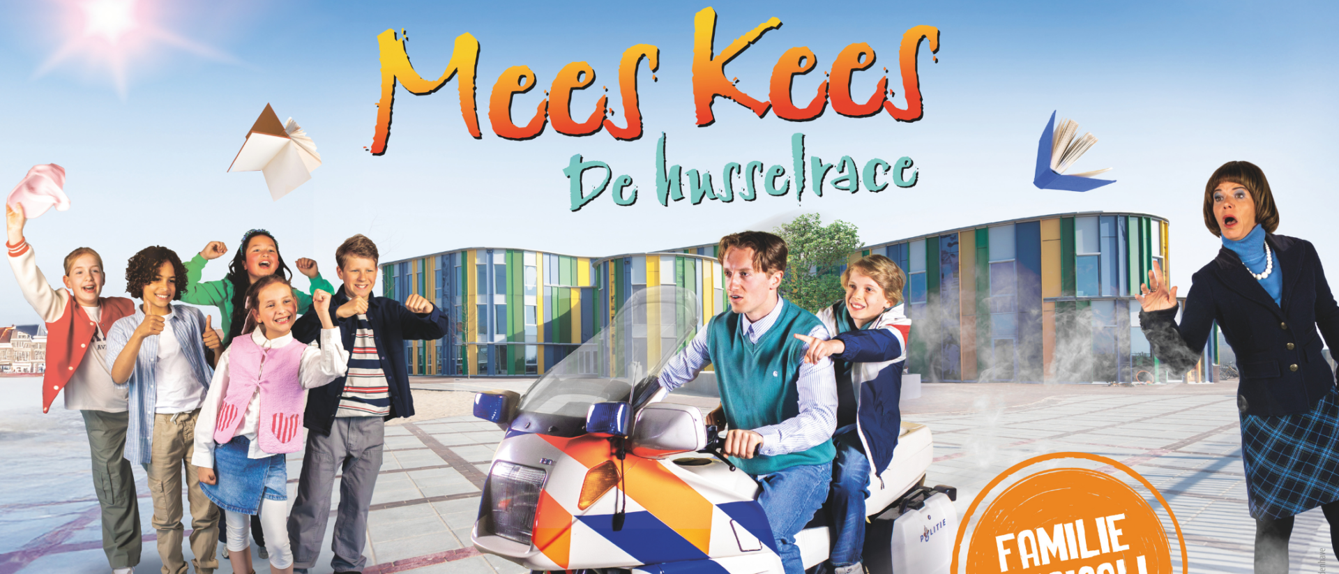 Vrolijke scène uit de familiemusical Mees Kees – De Husselrace, met kinderen die juichen, Mees Kees op een politiebrommer met een leerling achterop, en een verbaasde juf op de achtergrond voor een kleurrijk schoolgebouw.