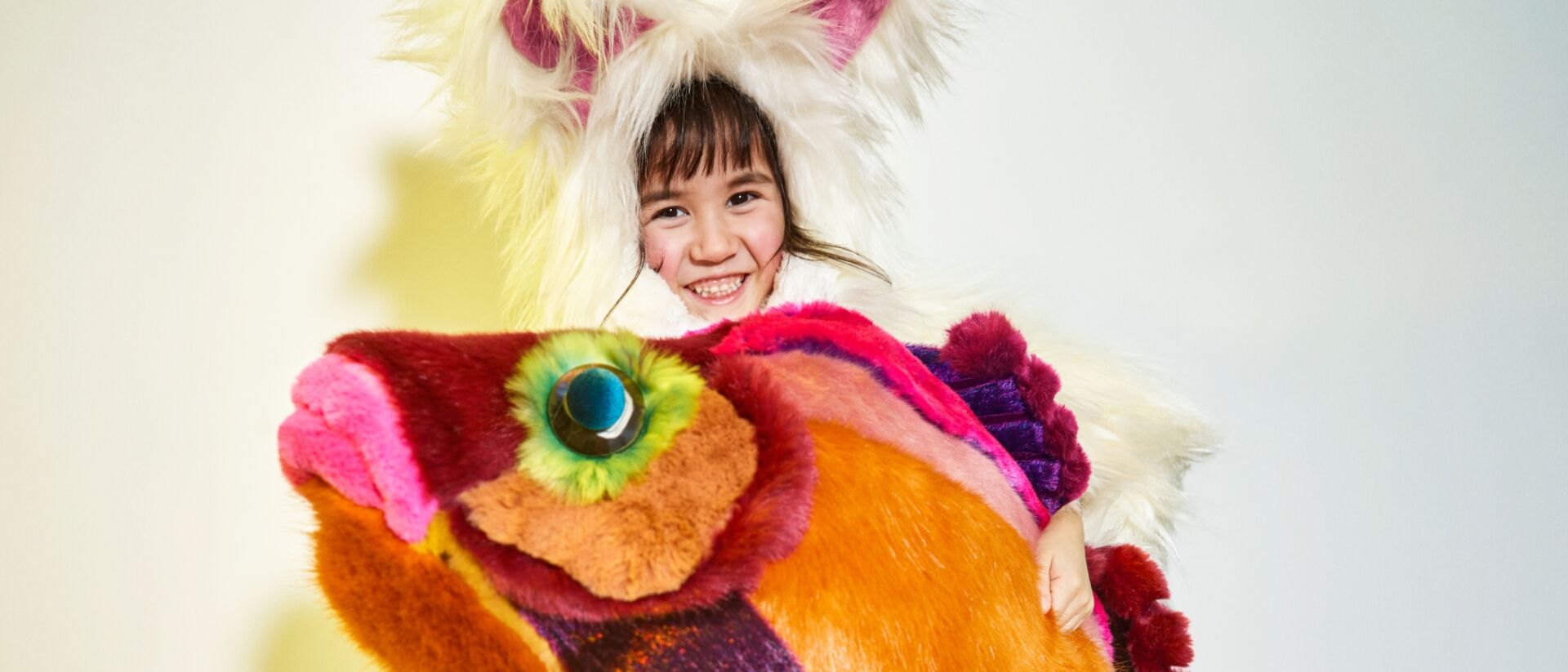 Een kind in een fluffy pak met in haar hand een knuffel in de vorm van een vis.