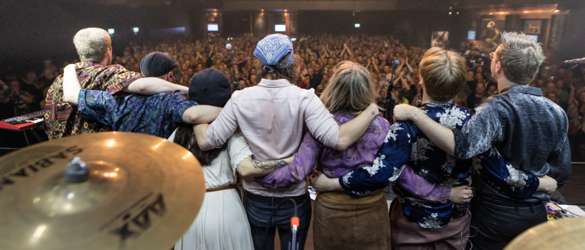 De band gaat bijna buigen naar het publiek en is van achteren gefotografeerd.