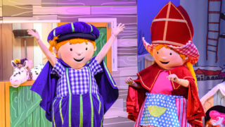 Fien en Teun als grote poppen in kleurrijke kostuums, met Fien in een Sinterklaaspak en Teun in een Pieten pak, op een vrolijk podium met dierenhoofden op de achtergrond.