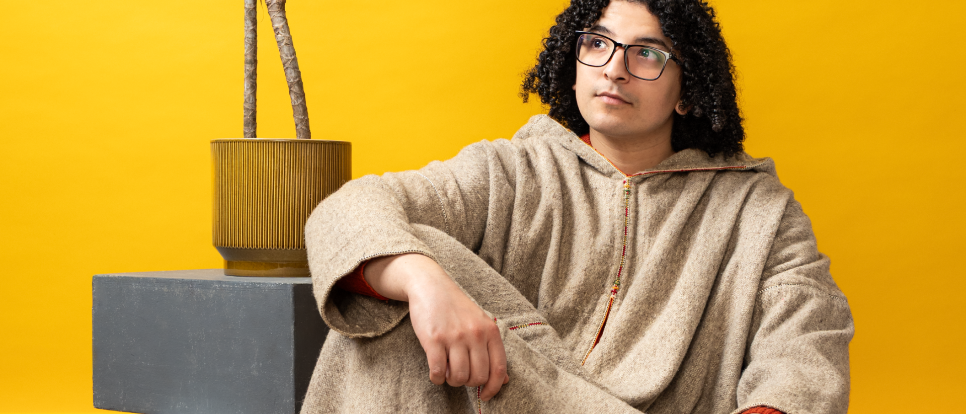 Ayoub Kharkhach kijkend naar boven met een plant op de achtergrond en een gele muur