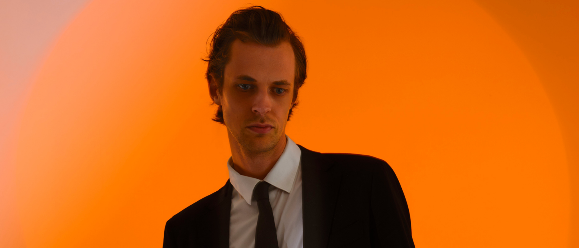 David Linszen leunend op een heup met een oranje achtergrond