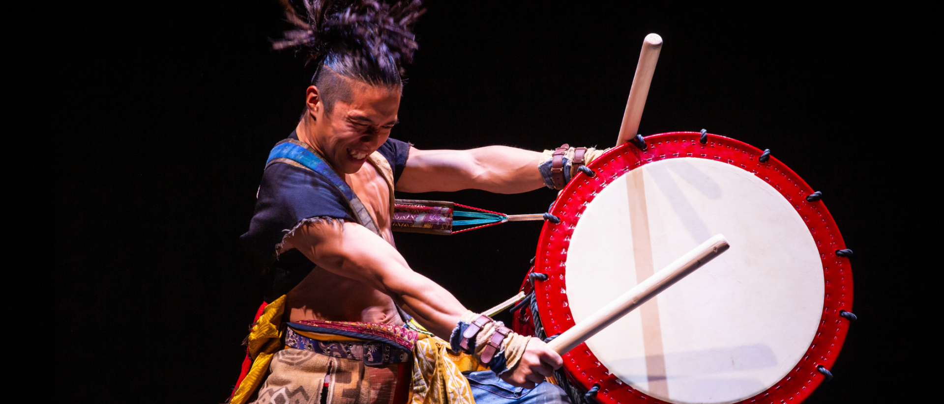 Een drummer die fanatiek op een enorme drum slaat met stokken in zijn handen