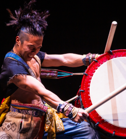 Een drummer die fanatiek op een enorme drum slaat met stokken in zijn handen