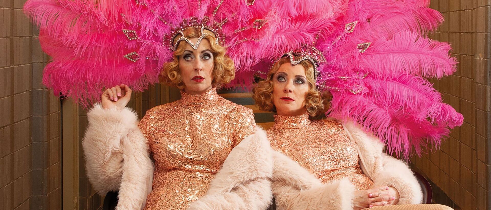 Plien & Bianca zitten in een glitterpak met roze veren op hun hoofd