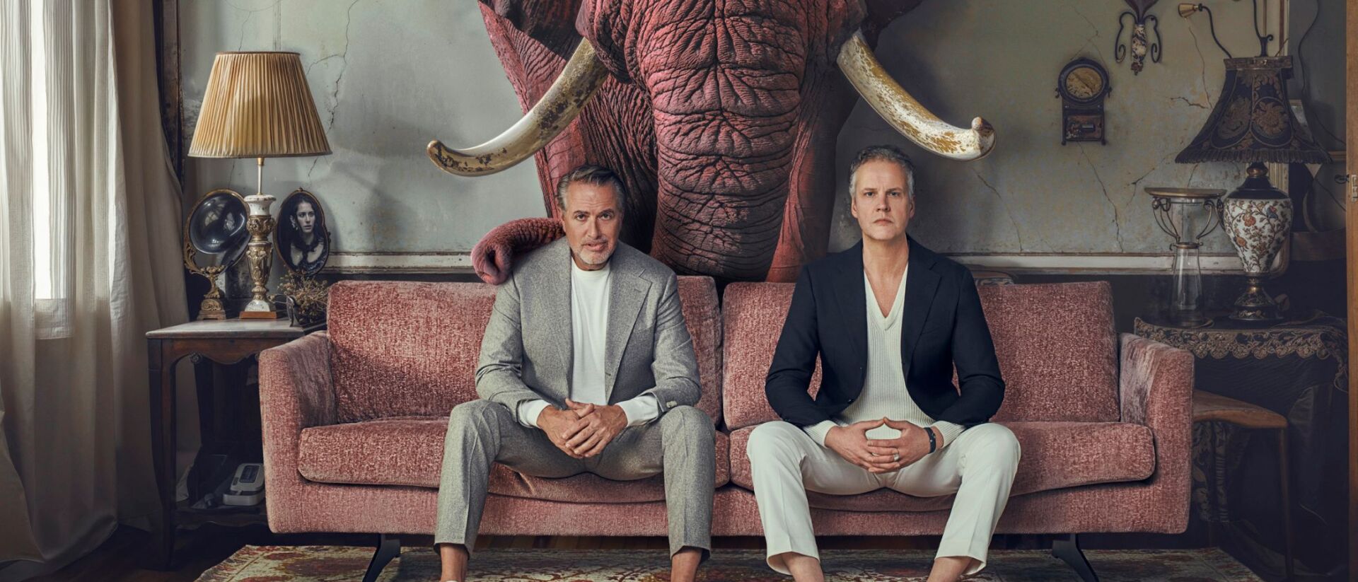 Veldhuis en Kemper zitten op een bank. Achter hu zie je op de muur een afbeelding van een grote olifant.