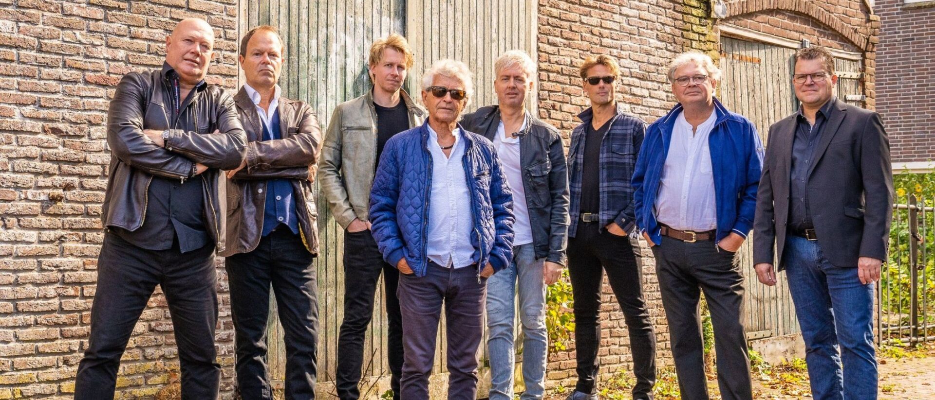 Je ziet de bandleden op een rij staan.