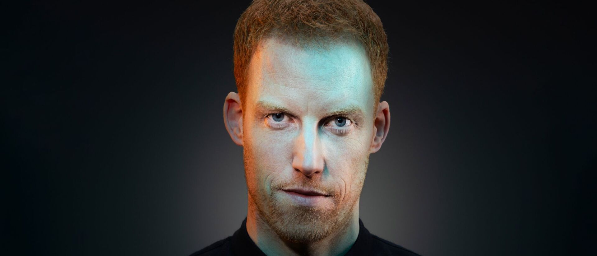 Portret van René van Meurs met een intense blik, verlicht door zachte blauwe en groene lichten op een donkere achtergrond