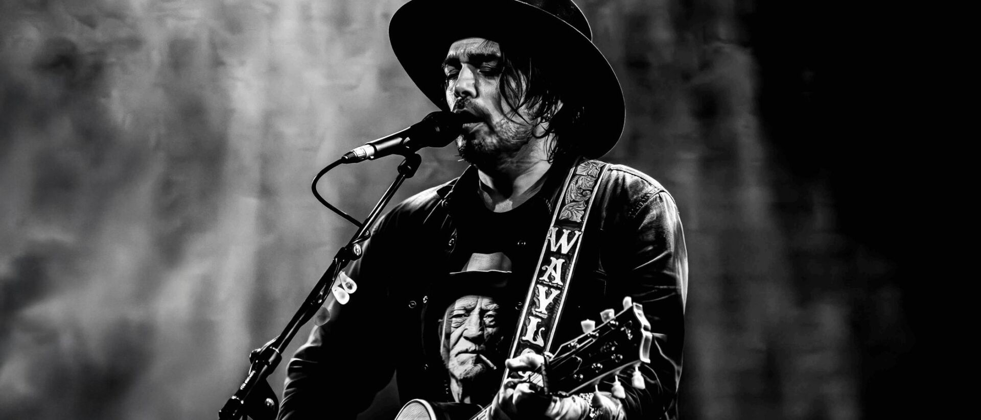 Waylon voert live op met een gitaar en microfoon, draagt een zwarte hoed