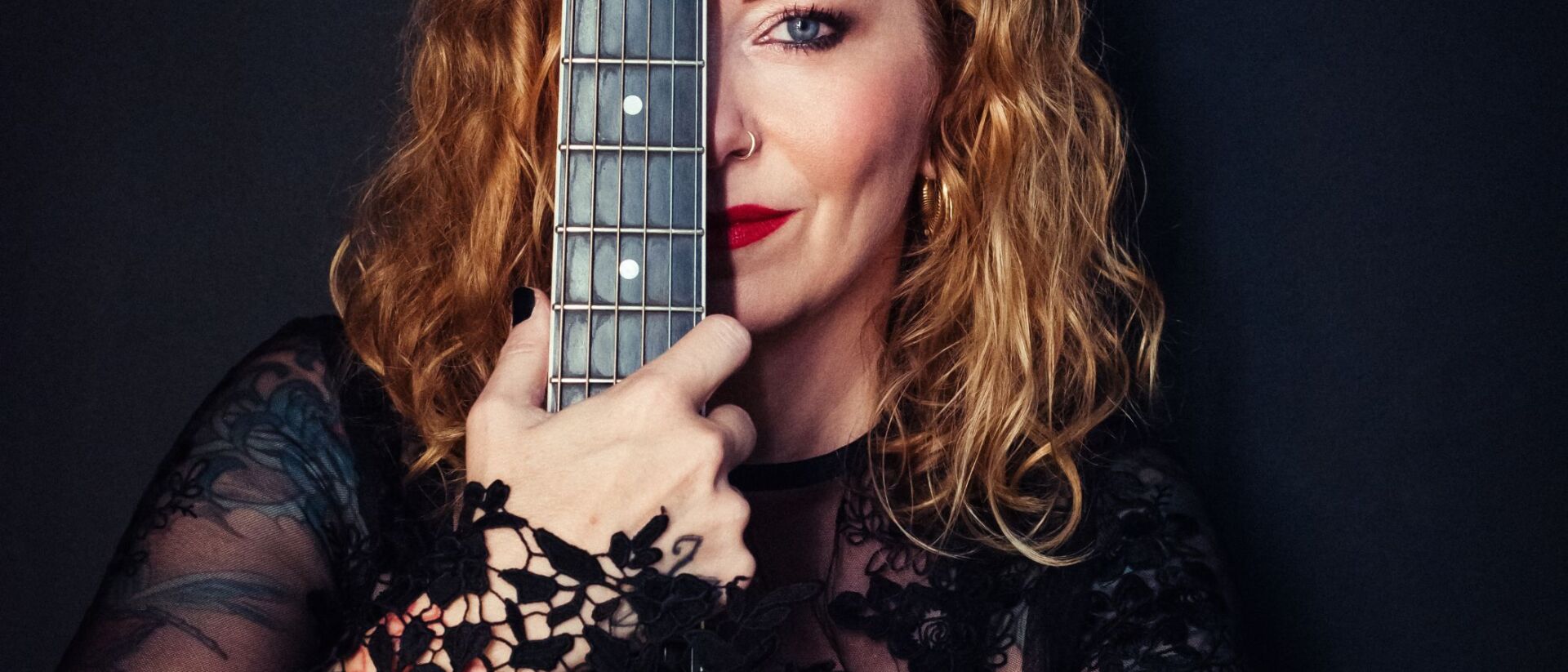 Anneke van Giersbergen houdt een gitaar voor haar gezicht, met een glimlach.
