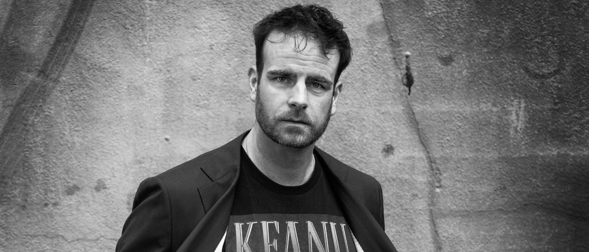 Henry van Loon kijkt in de camera en toont zijn t shirt.