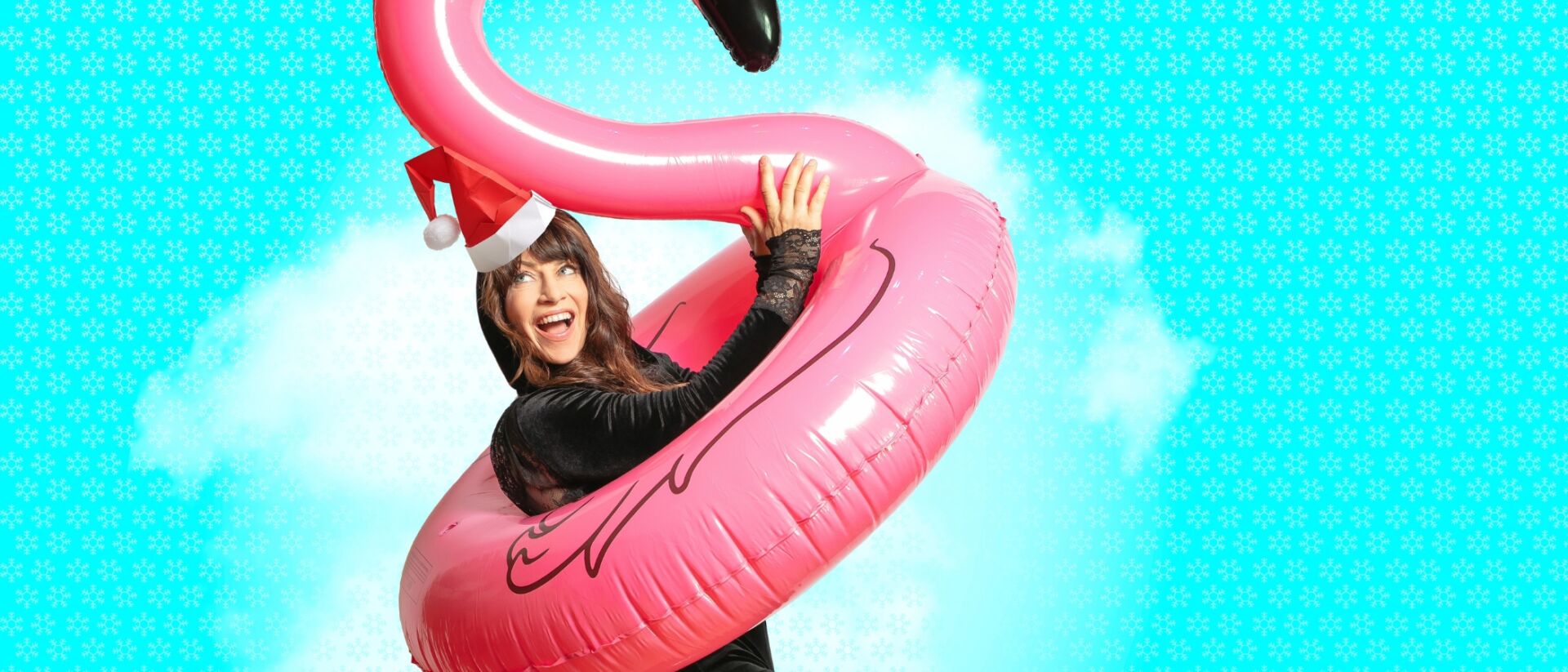 Ellen ten Damme met om haar heen een opblaas flamingo zwemband en op haar hoofd een kerstmuts.