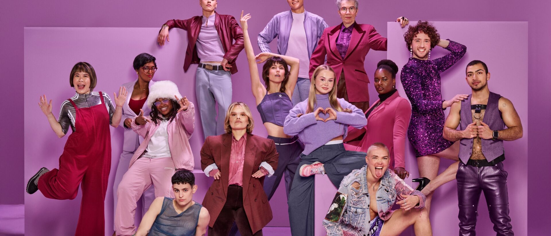Een groep personen die de camera inkijken met veel paarse en roze kleding en een paarse achtergrond.