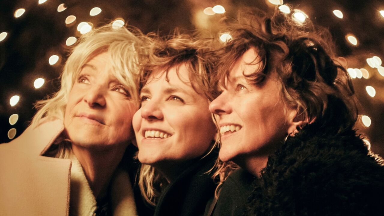 Drie vrouwen die links naar boven kijken met op de achtergrond lichtjes.