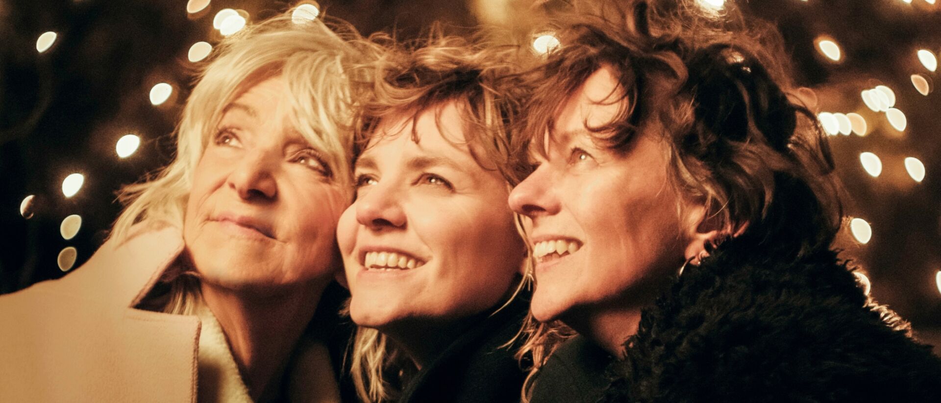 Drie vrouwen die links naar boven kijken met op de achtergrond lichtjes.