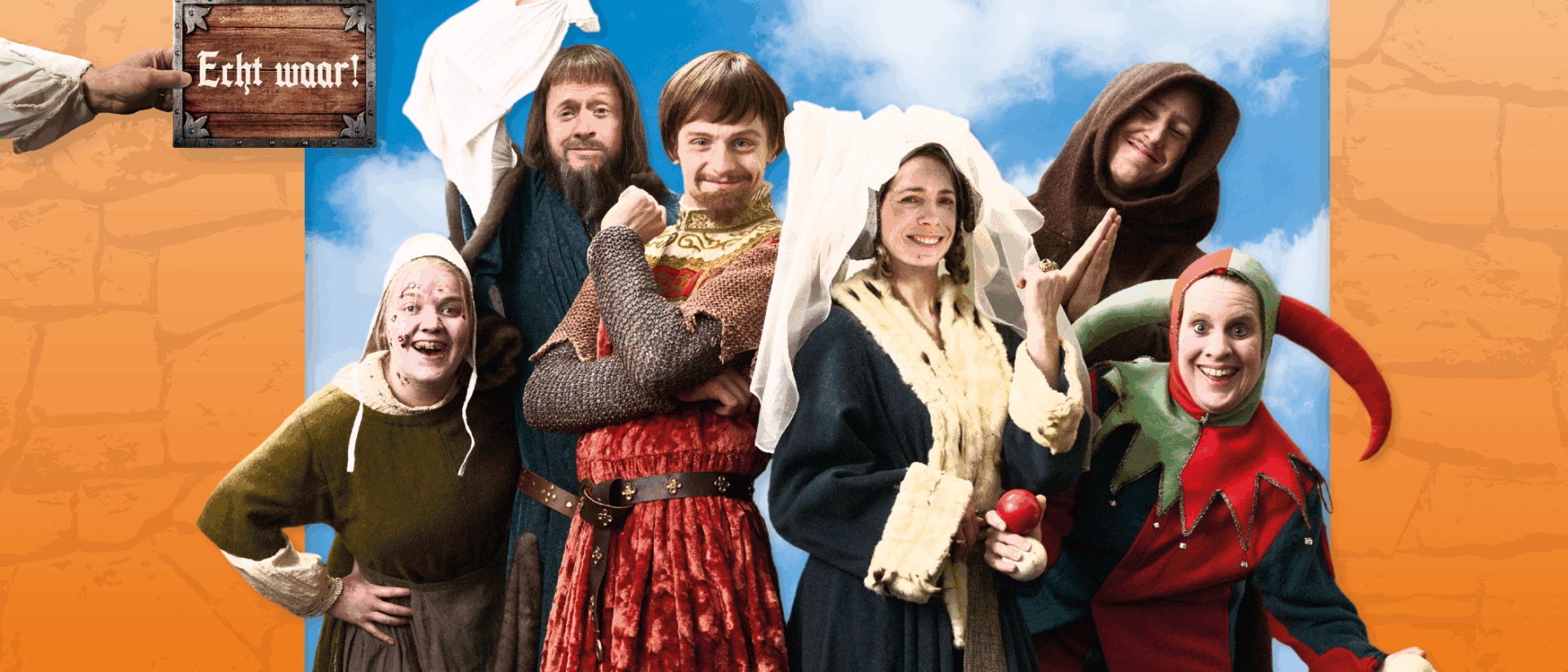 Een kasteel tegen een blauwe lucht. De cast staat in kostuum op de voorgrond.