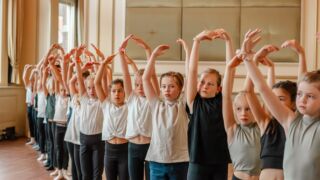 Kinderen op een rij met handen omhoog die ballet doen