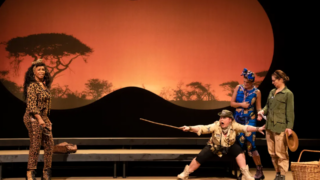 Vier acteurs in een komische theatervoorstelling met een Afrikaanse savanne als decor.