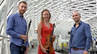Drie personen die staan bij een metrohalte waarvan twee een instrument vasthouden
