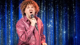 Meneer die aan het zingen is in een microfoon bij een piano