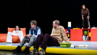 2 mannen zitten op een verhoging met een vrouw op de achtergrond