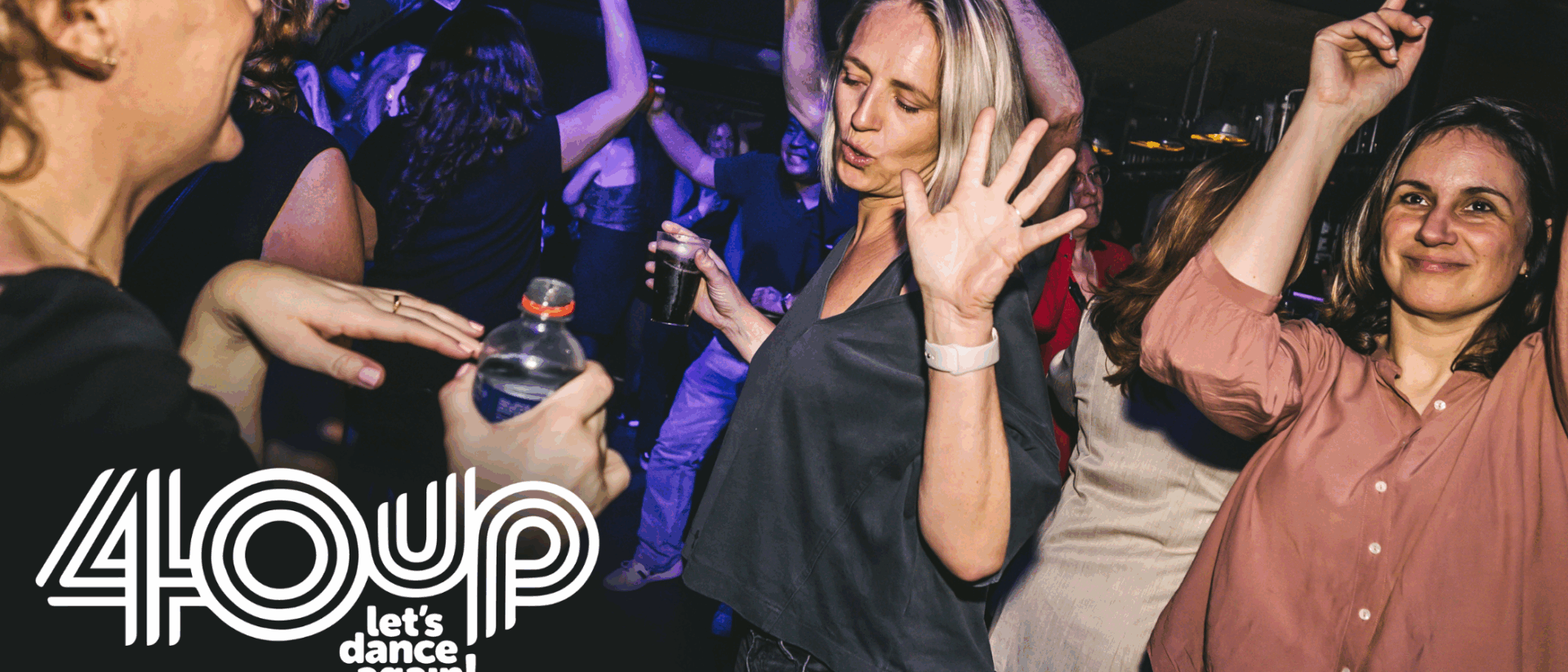 Mensen dansen en genieten op een 40UP-feest, met vrolijke gezichten en handen in de lucht op de dansvloer