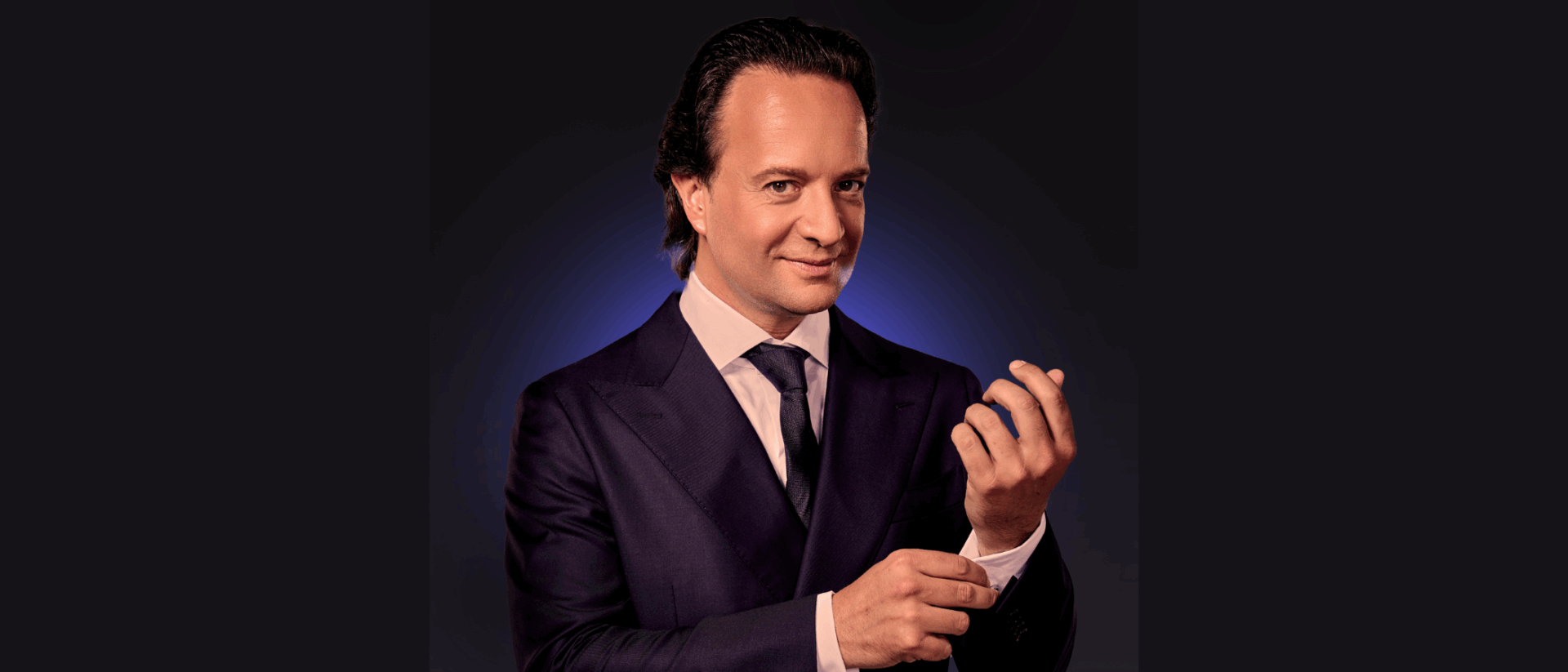 William Janz kijkt in de camera terwijl hij het knoopje van zijn mouw goed doet.