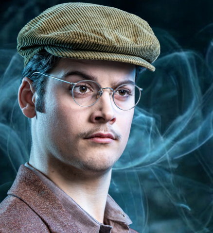 Benjamin Jas als Sebastian met pet en bril houdt boeken vast in musical Sherlock Holmes