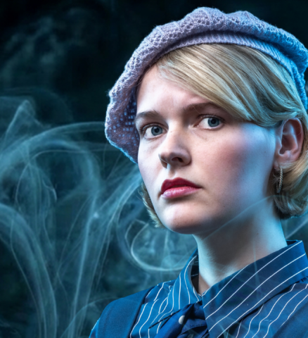 Loïs Senger als Nora Bennet in blauw gestreept kostuum met baret in Sherlock Holmes