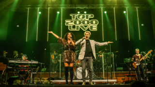 Twee zangers met band op groen verlicht podium tijdens Top 2000 Live Hoorn